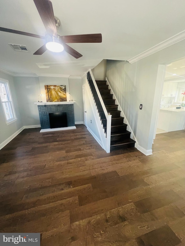 unfurnished living room with a fireplace, ceiling fan, crown molding, and dark wood-type flooring