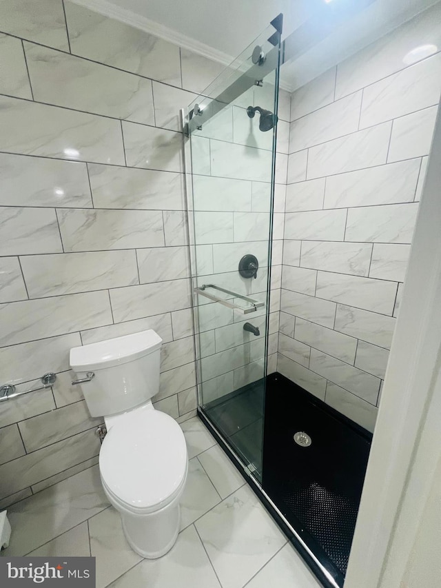 bathroom featuring toilet, ornamental molding, a shower with shower door, and tile walls