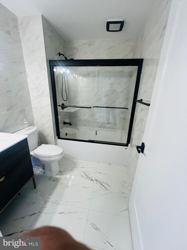 full bathroom featuring toilet, bath / shower combo with glass door, tile walls, and vanity