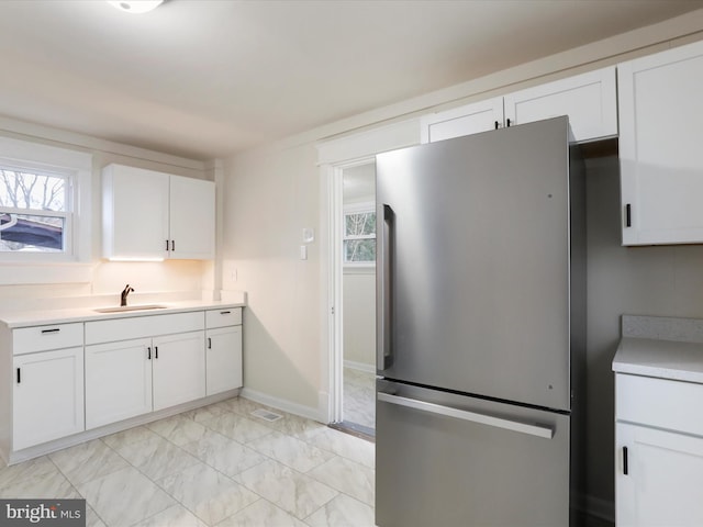 kitchen with white cabinetry, sink, and stainless steel refrigerator