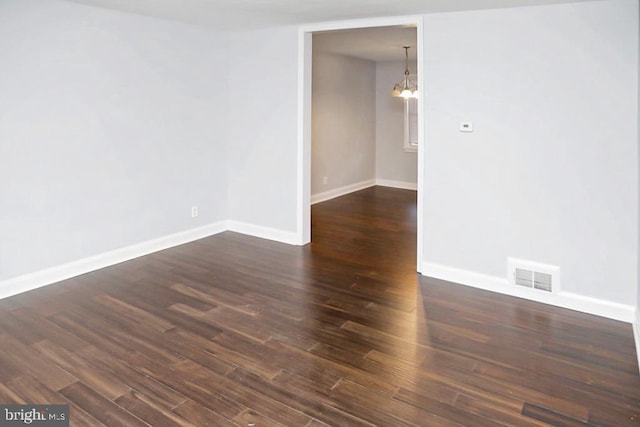 empty room with a notable chandelier and dark hardwood / wood-style flooring