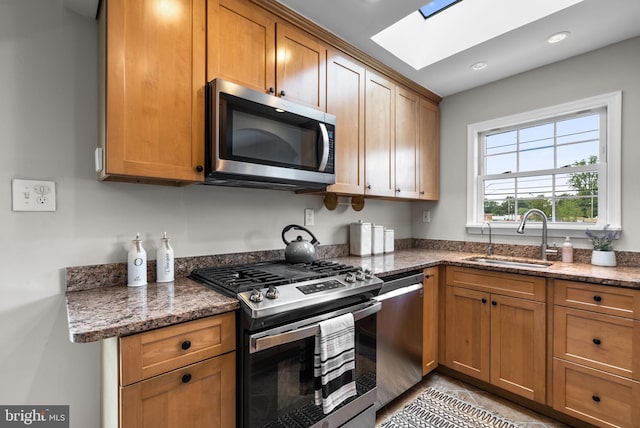 kitchen with sink, stainless steel appliances, a skylight, and dark stone counters