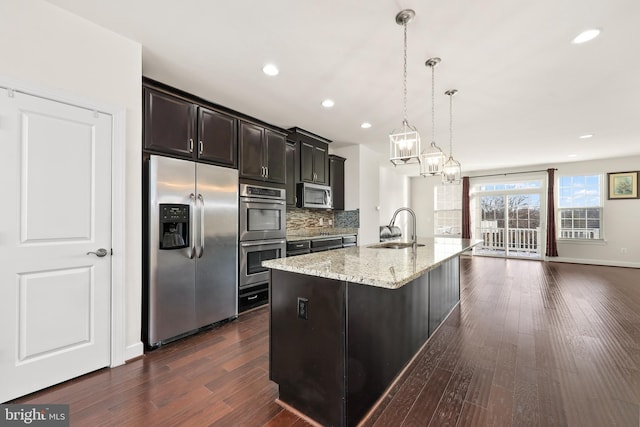 kitchen featuring hanging light fixtures, dark hardwood / wood-style flooring, sink, appliances with stainless steel finishes, and a kitchen island with sink