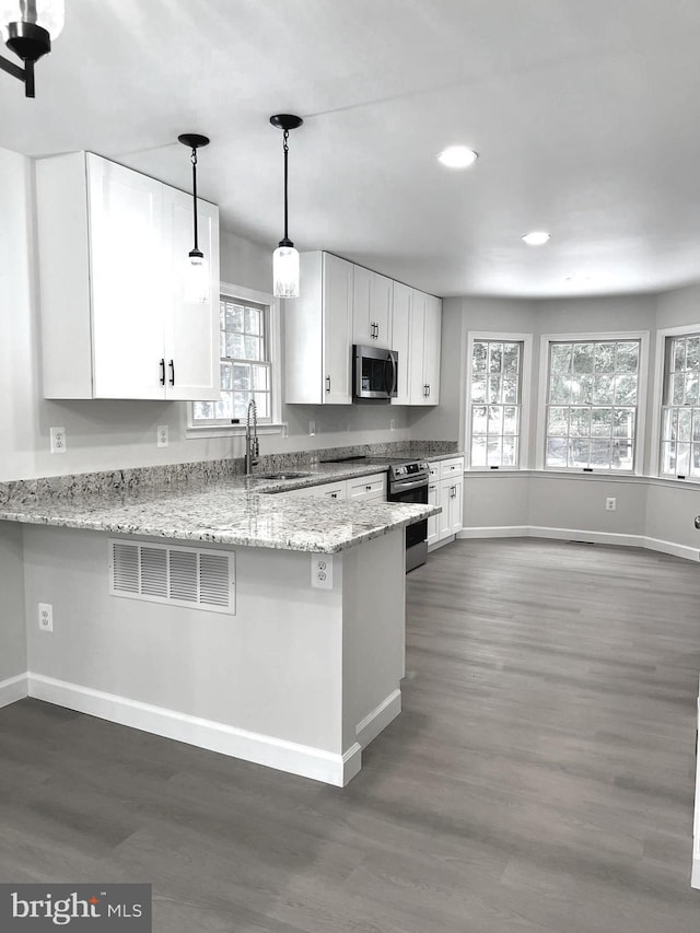 kitchen with light stone counters, kitchen peninsula, hanging light fixtures, white cabinetry, and appliances with stainless steel finishes