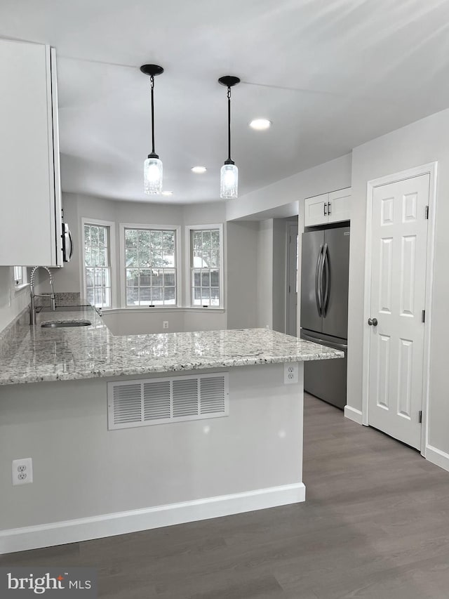 kitchen with stainless steel refrigerator, hanging light fixtures, kitchen peninsula, sink, and white cabinetry