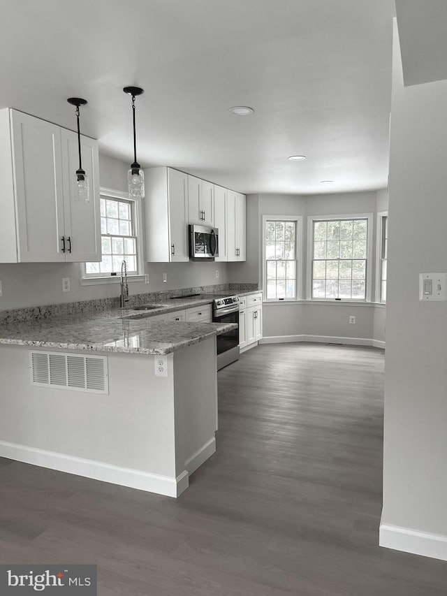 kitchen featuring stainless steel appliances, kitchen peninsula, light stone countertops, sink, and white cabinetry