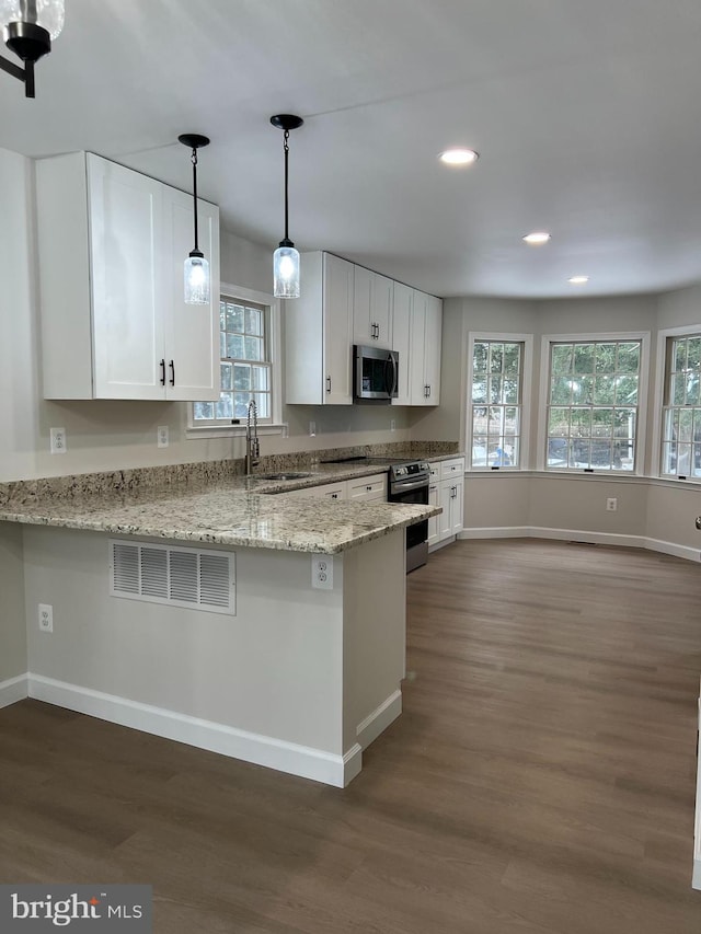 kitchen featuring appliances with stainless steel finishes, kitchen peninsula, dark hardwood / wood-style flooring, light stone counters, and white cabinetry