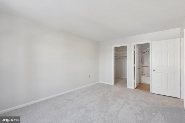 unfurnished bedroom featuring ensuite bath, light carpet, a spacious closet, and a closet