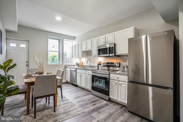 kitchen featuring stainless steel appliances, sink, white cabinetry, light hardwood / wood-style flooring, and light stone countertops