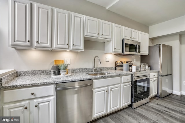 kitchen featuring stainless steel appliances, sink, white cabinets, light stone counters, and light hardwood / wood-style flooring