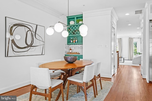 dining area with bar area, ornamental molding, and hardwood / wood-style floors