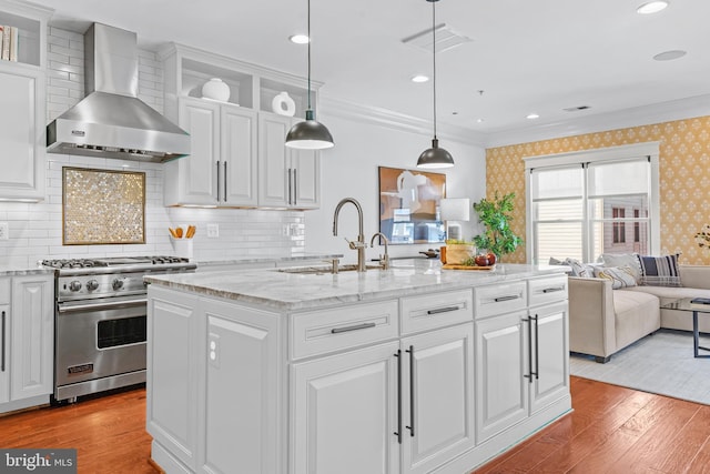 kitchen featuring white cabinetry, a kitchen island with sink, wall chimney exhaust hood, and designer stove