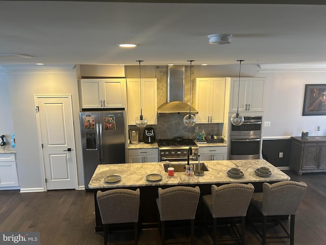 kitchen featuring backsplash, wall chimney range hood, appliances with stainless steel finishes, an island with sink, and light stone counters