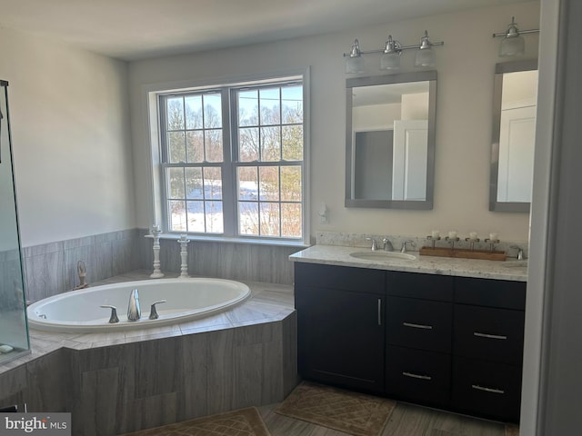 bathroom with tiled bath, vanity, and a healthy amount of sunlight