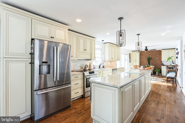 kitchen with light stone countertops, appliances with stainless steel finishes, hanging light fixtures, cream cabinetry, and dark hardwood / wood-style flooring