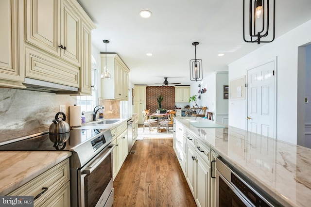 kitchen featuring light stone countertops, hanging light fixtures, cream cabinetry, and stainless steel range with electric stovetop