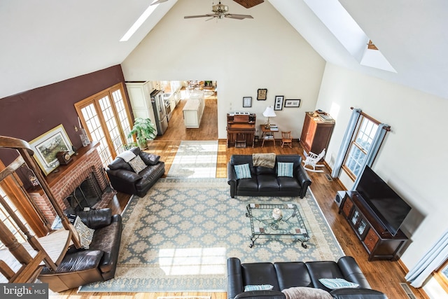 living room with hardwood / wood-style floors, a fireplace, a skylight, high vaulted ceiling, and ceiling fan