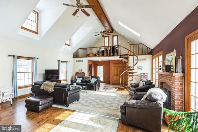 living room featuring a towering ceiling, beamed ceiling, wood-type flooring, a skylight, and a brick fireplace