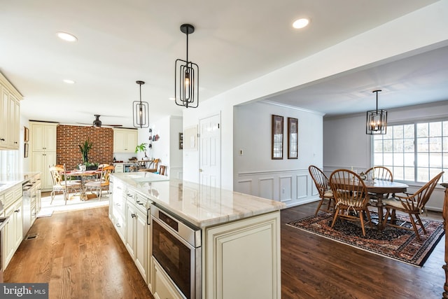 kitchen with cream cabinetry, a center island, hanging light fixtures, and light stone countertops