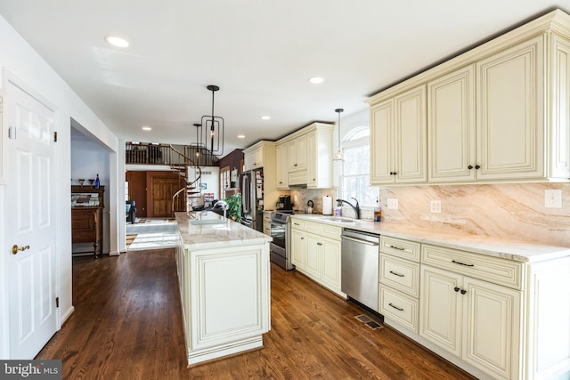 kitchen featuring cream cabinets, a center island, pendant lighting, dark wood-type flooring, and stainless steel appliances