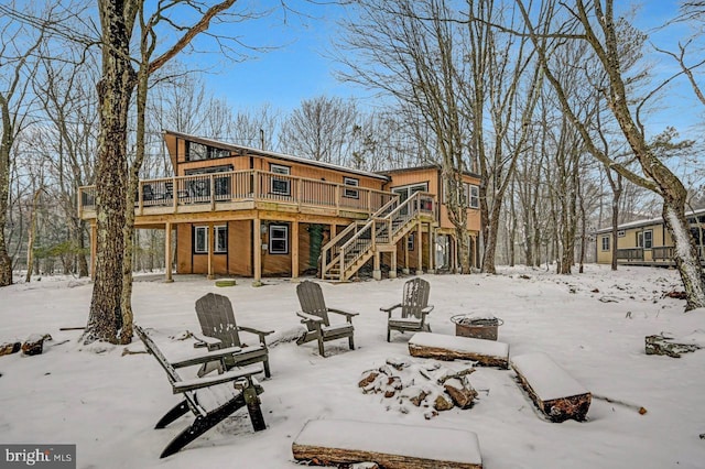 snow covered back of property with a wooden deck and a fire pit