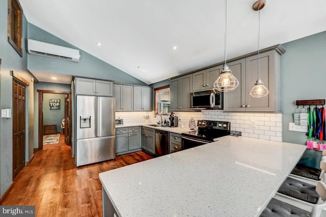 kitchen featuring pendant lighting, appliances with stainless steel finishes, tasteful backsplash, vaulted ceiling, and a wall mounted air conditioner