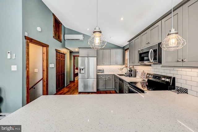 kitchen with vaulted ceiling, gray cabinets, a wall mounted air conditioner, hanging light fixtures, and appliances with stainless steel finishes