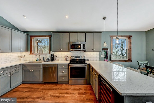 kitchen with appliances with stainless steel finishes, wine cooler, hanging light fixtures, light stone countertops, and sink