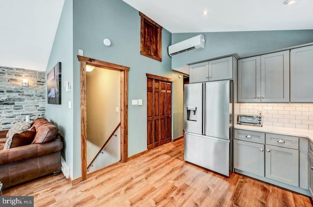 kitchen with stainless steel refrigerator with ice dispenser, gray cabinetry, lofted ceiling, and an AC wall unit