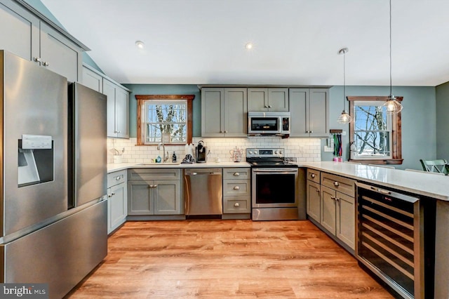 kitchen with appliances with stainless steel finishes, light wood-type flooring, wine cooler, pendant lighting, and sink