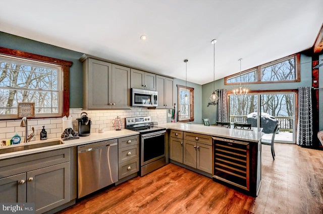 kitchen with appliances with stainless steel finishes, decorative light fixtures, wine cooler, sink, and kitchen peninsula