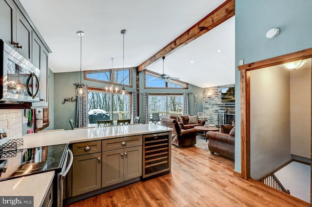 kitchen with ceiling fan with notable chandelier, stainless steel appliances, a stone fireplace, wine cooler, and beam ceiling