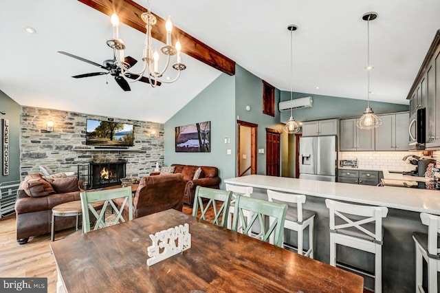 dining area featuring a stone fireplace, high vaulted ceiling, light wood-type flooring, ceiling fan, and beam ceiling