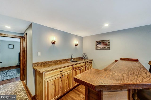 kitchen featuring light hardwood / wood-style floors, kitchen peninsula, light stone counters, and sink