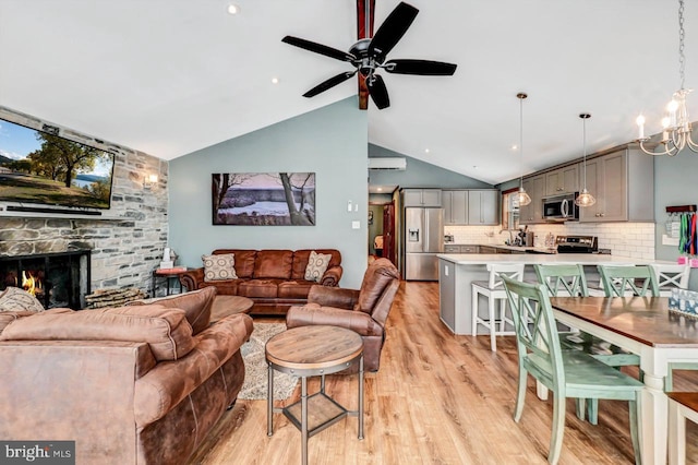 living room with light wood-type flooring, lofted ceiling, ceiling fan with notable chandelier, and a stone fireplace