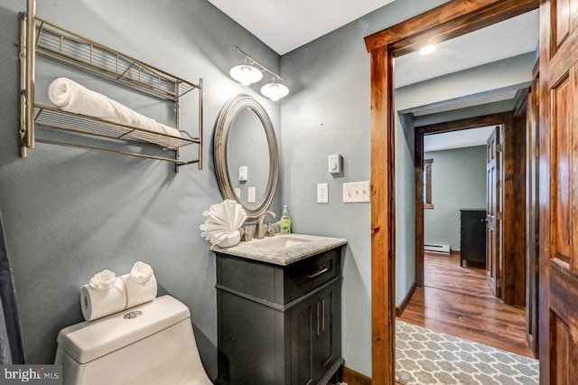 bathroom with toilet, baseboard heating, hardwood / wood-style floors, and vanity