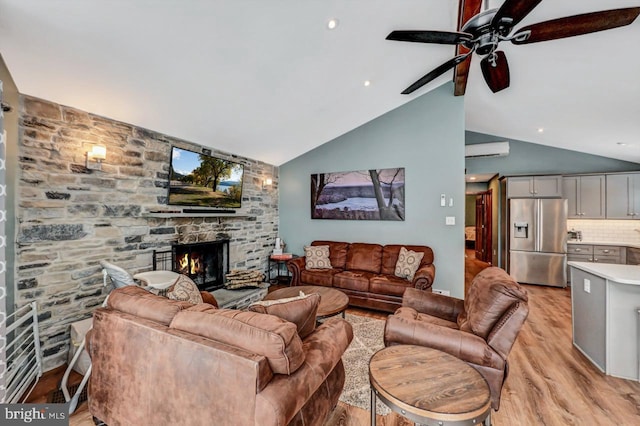 living room with ceiling fan, vaulted ceiling, a stone fireplace, and light hardwood / wood-style floors