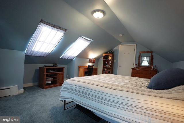 carpeted bedroom with a baseboard heating unit and vaulted ceiling