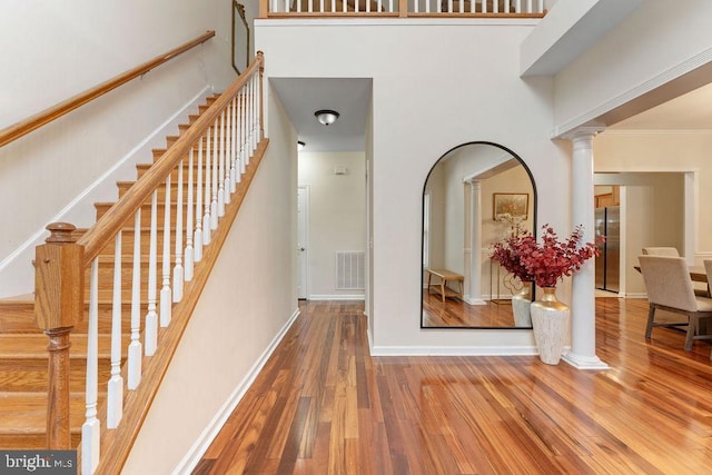 staircase with decorative columns, a high ceiling, and hardwood / wood-style floors