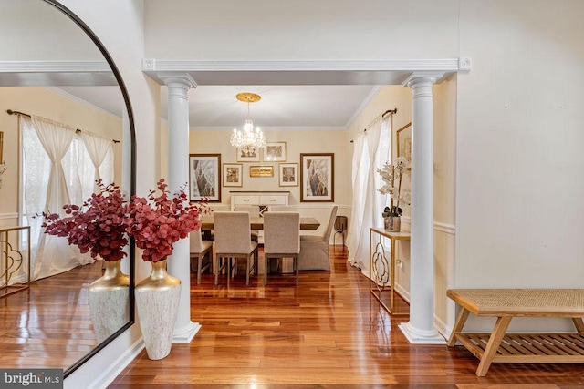 dining space with crown molding, wood-type flooring, an inviting chandelier, and decorative columns