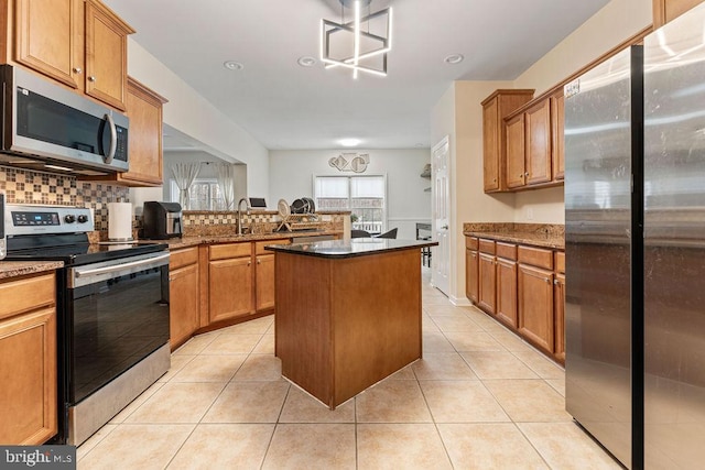 kitchen with a center island, light tile patterned flooring, sink, stainless steel appliances, and dark stone counters