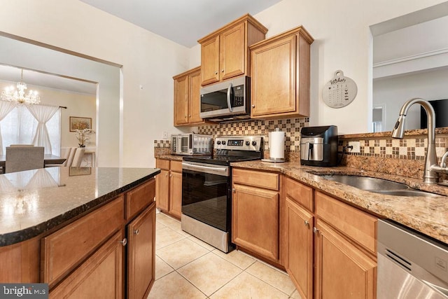 kitchen with sink, backsplash, appliances with stainless steel finishes, and a notable chandelier