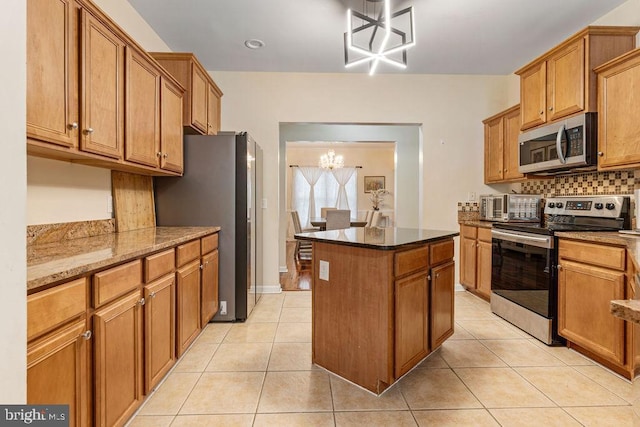 kitchen featuring a center island, stainless steel appliances, dark stone countertops, a notable chandelier, and light tile patterned floors