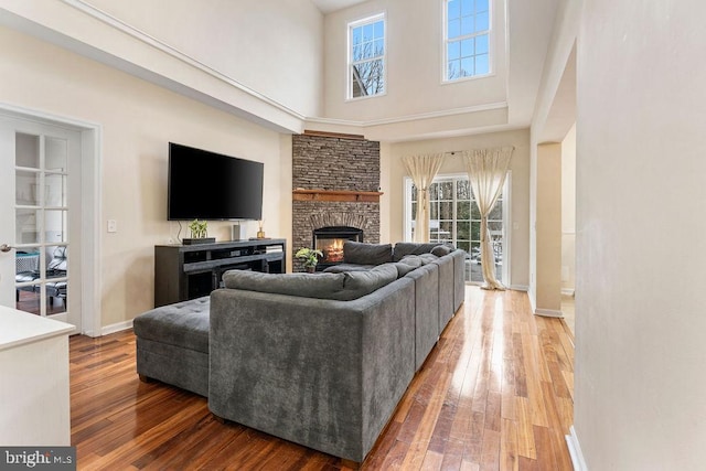 living room with a high ceiling, hardwood / wood-style flooring, and a stone fireplace