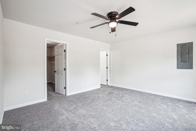 unfurnished bedroom featuring a closet, dark colored carpet, ceiling fan, electric panel, and a walk in closet