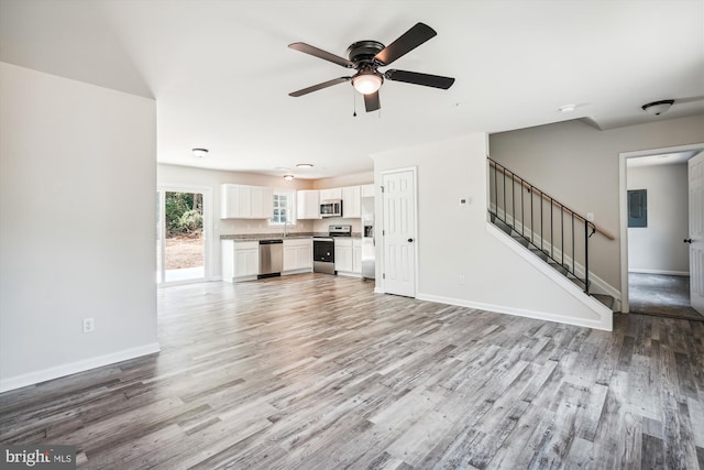 unfurnished living room featuring sink, ceiling fan, light hardwood / wood-style floors, and electric panel