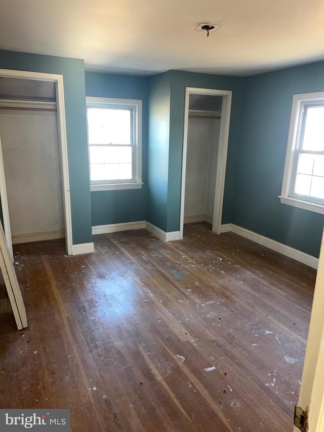 unfurnished bedroom featuring multiple closets and dark wood-type flooring