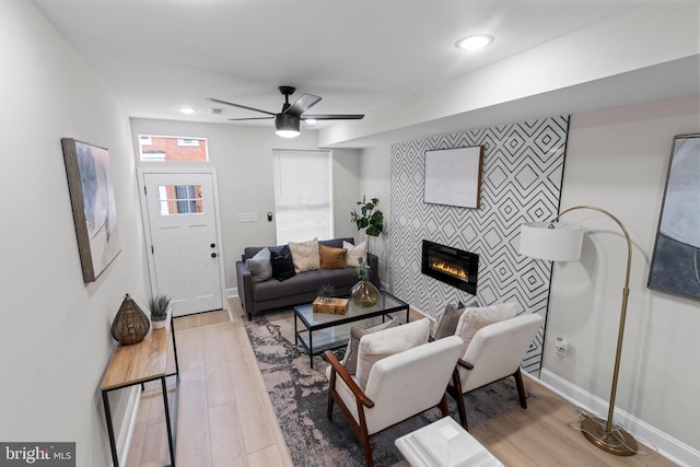 living room featuring a tile fireplace, ceiling fan, and light hardwood / wood-style floors