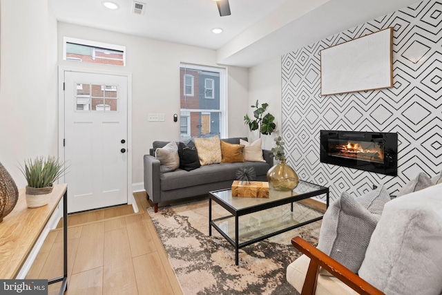 living room featuring a tile fireplace, ceiling fan, and light hardwood / wood-style flooring