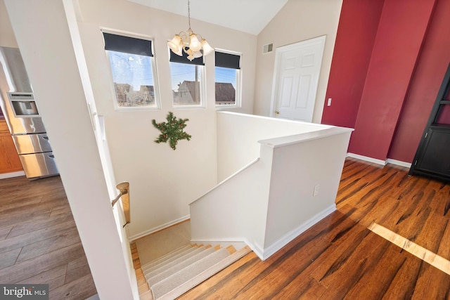 staircase featuring a notable chandelier, vaulted ceiling, and hardwood / wood-style flooring